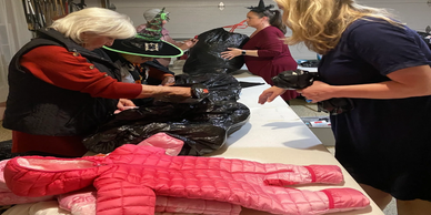 People crafting Halloween decorations with black bags and a pink costume on the table.
