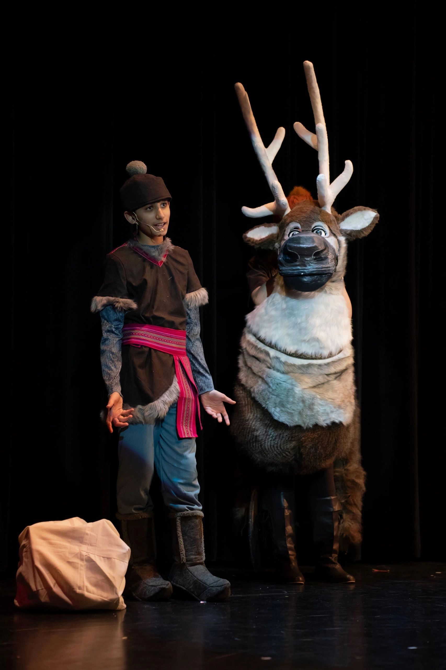 Actor in costume with reindeer on stage.