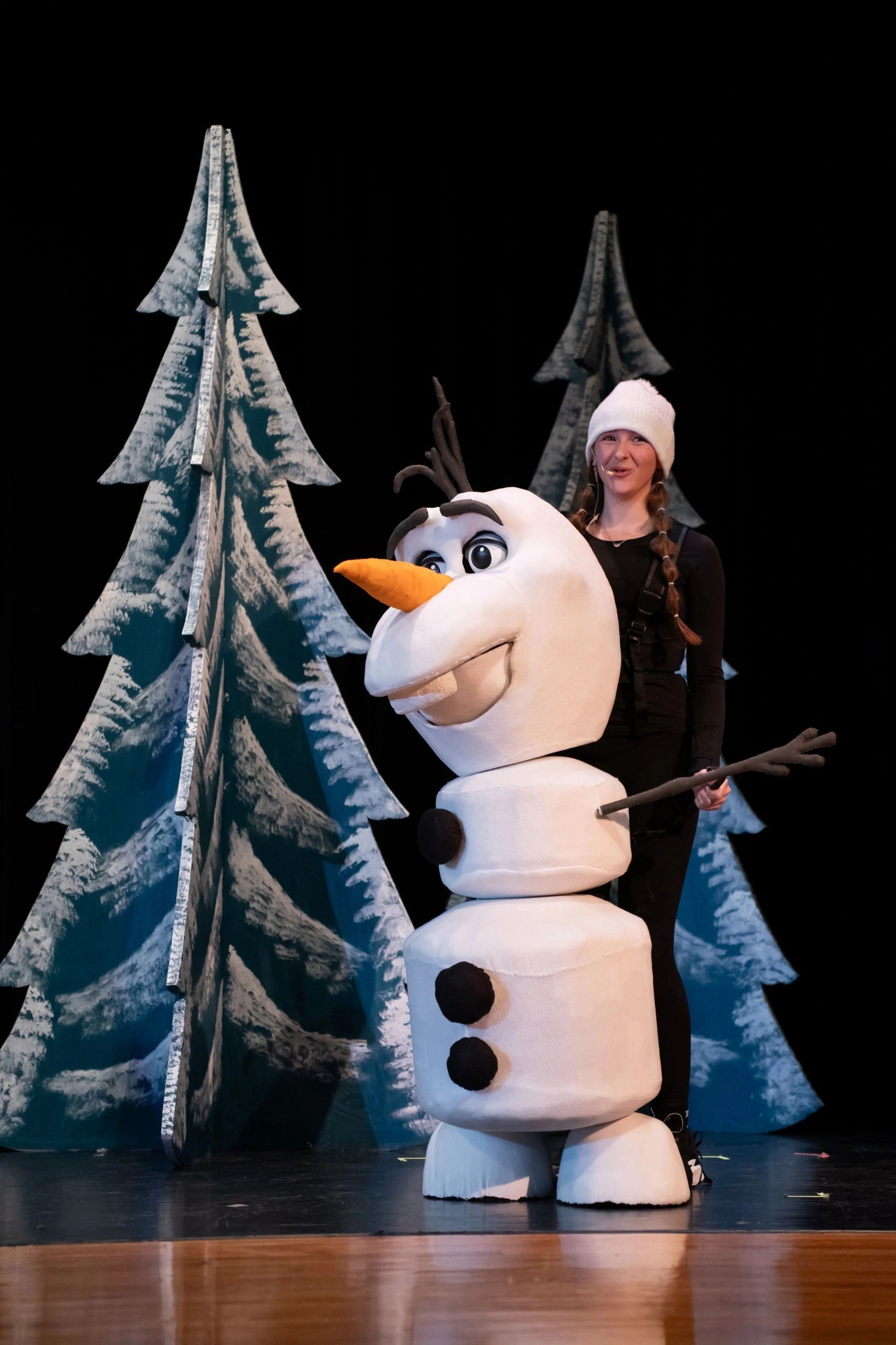 Person puppeteering a large snowman puppet on stage.