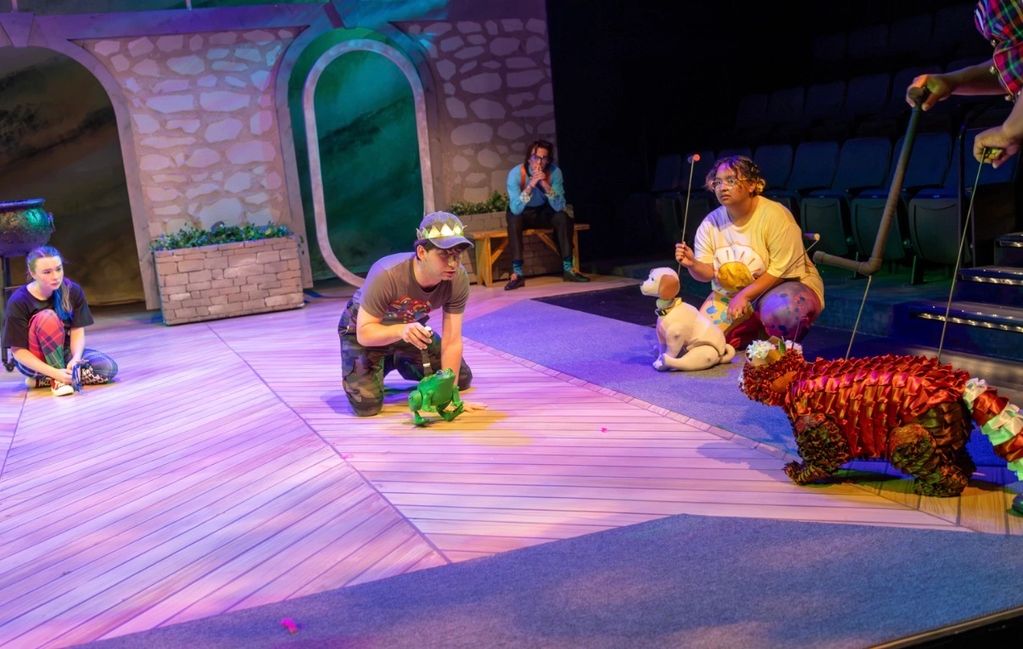 Actors manipulating animal puppets on stage in a colorful play.