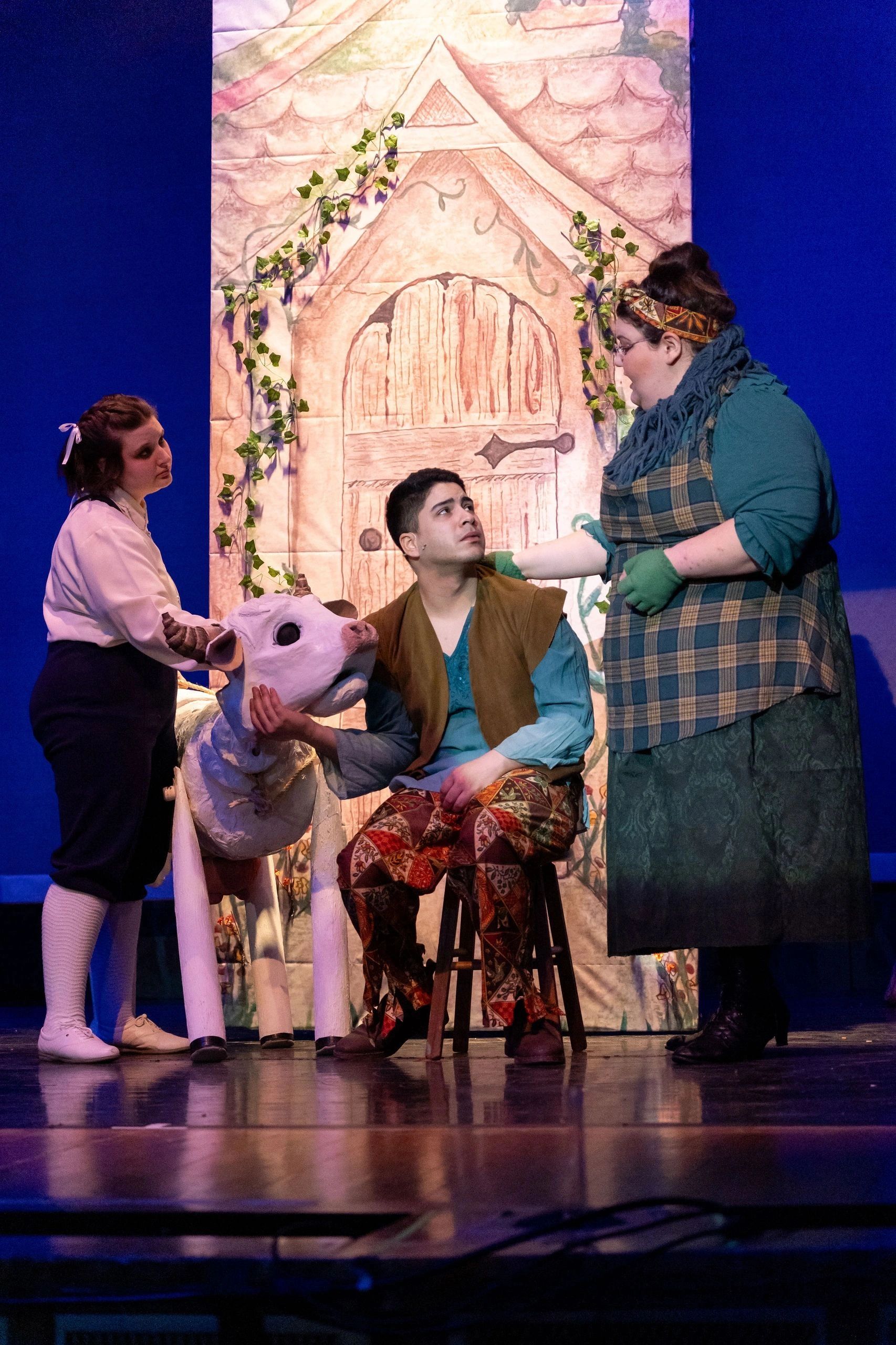 Actors performing with a puppet cow on stage.