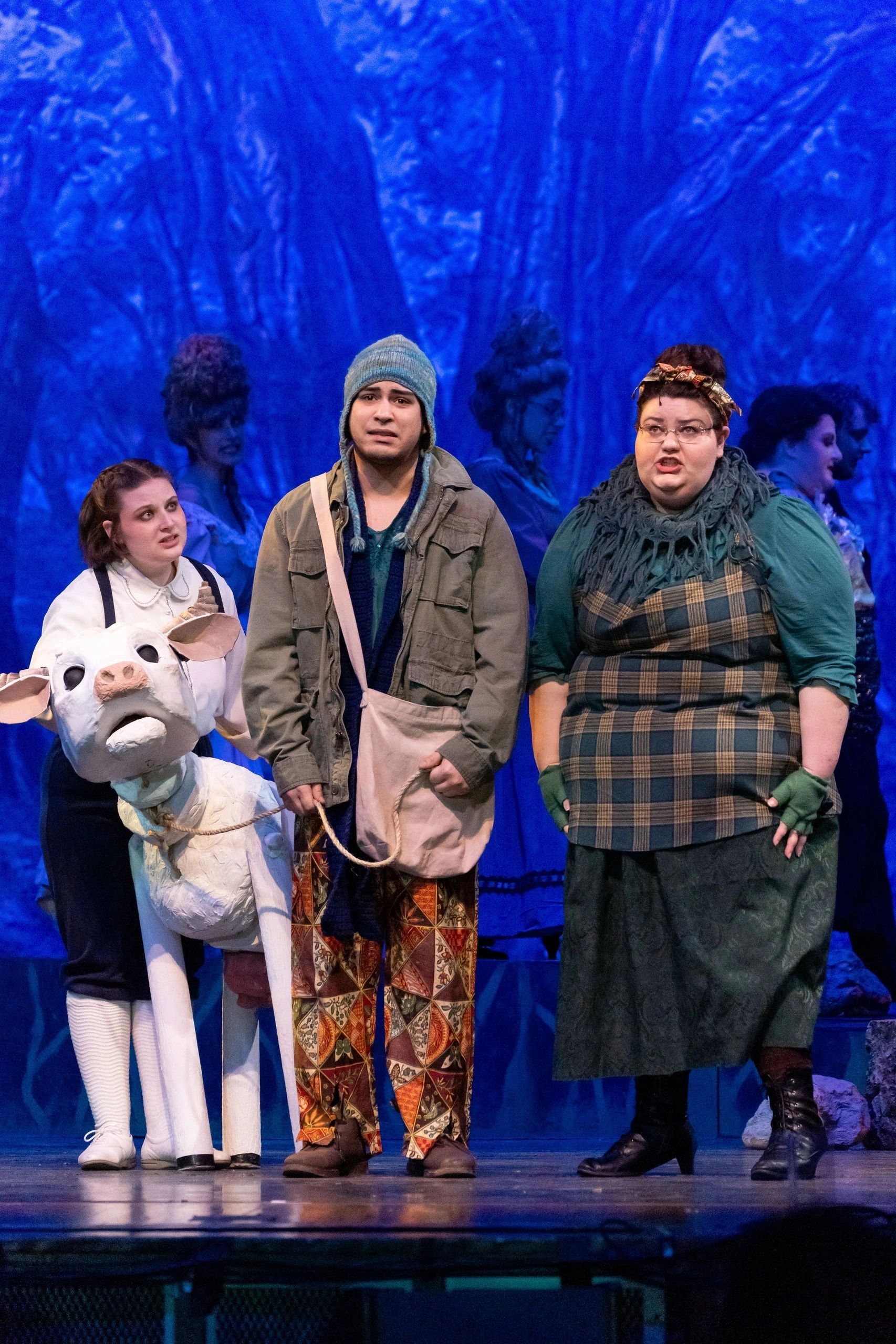 Three actors on stage with a puppet in a forest setting.
