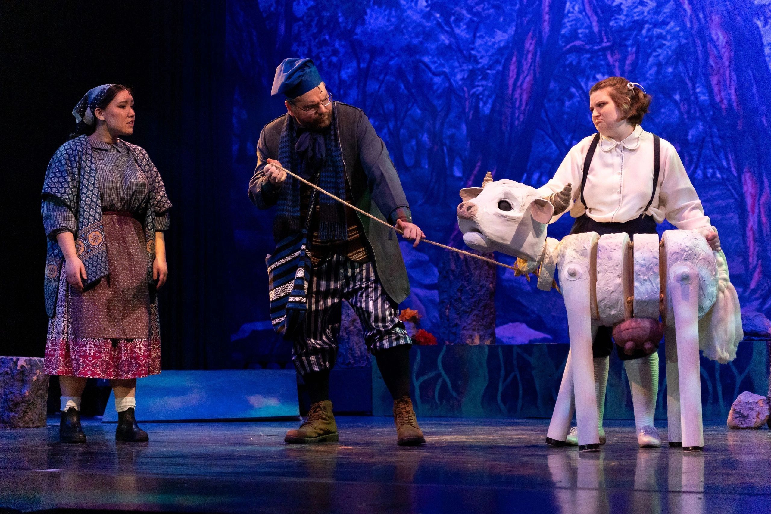 Actors performing with a cow puppet on stage.