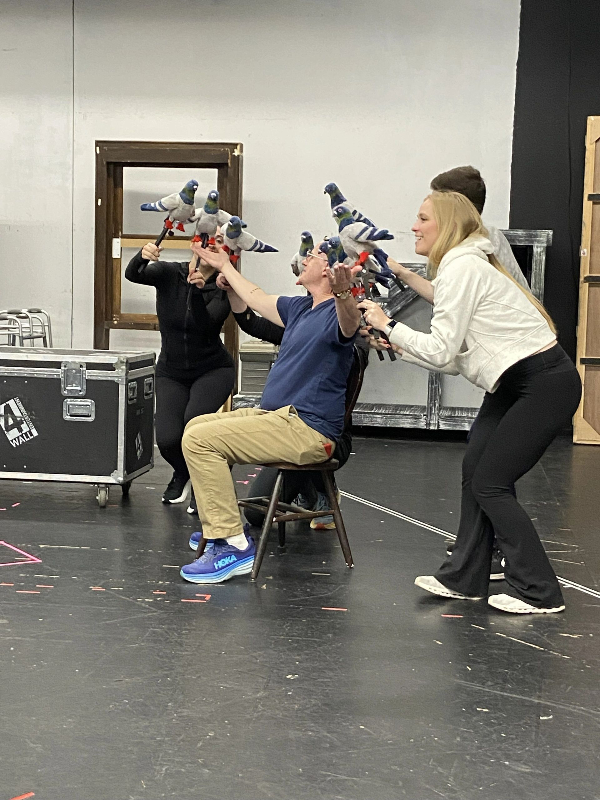 Four people with fake bird puppets in a rehearsal space.