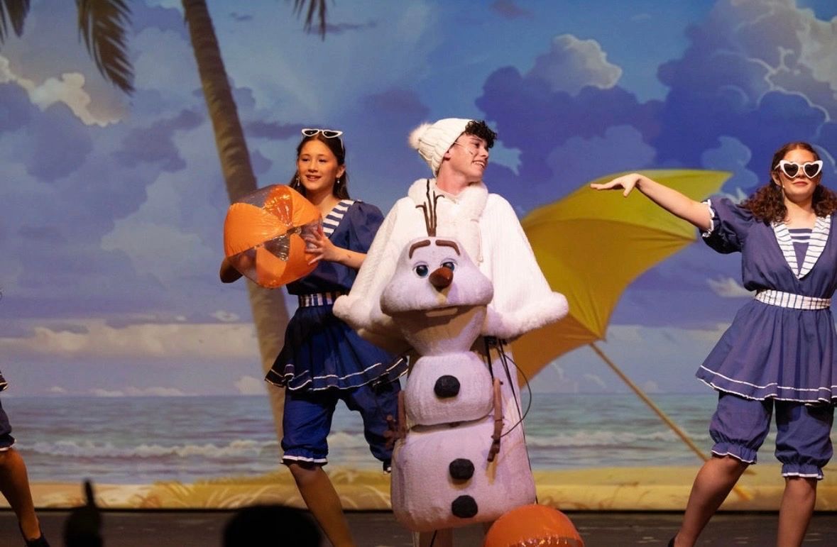 Actors performing in beach-themed costumes with a snowman character.
