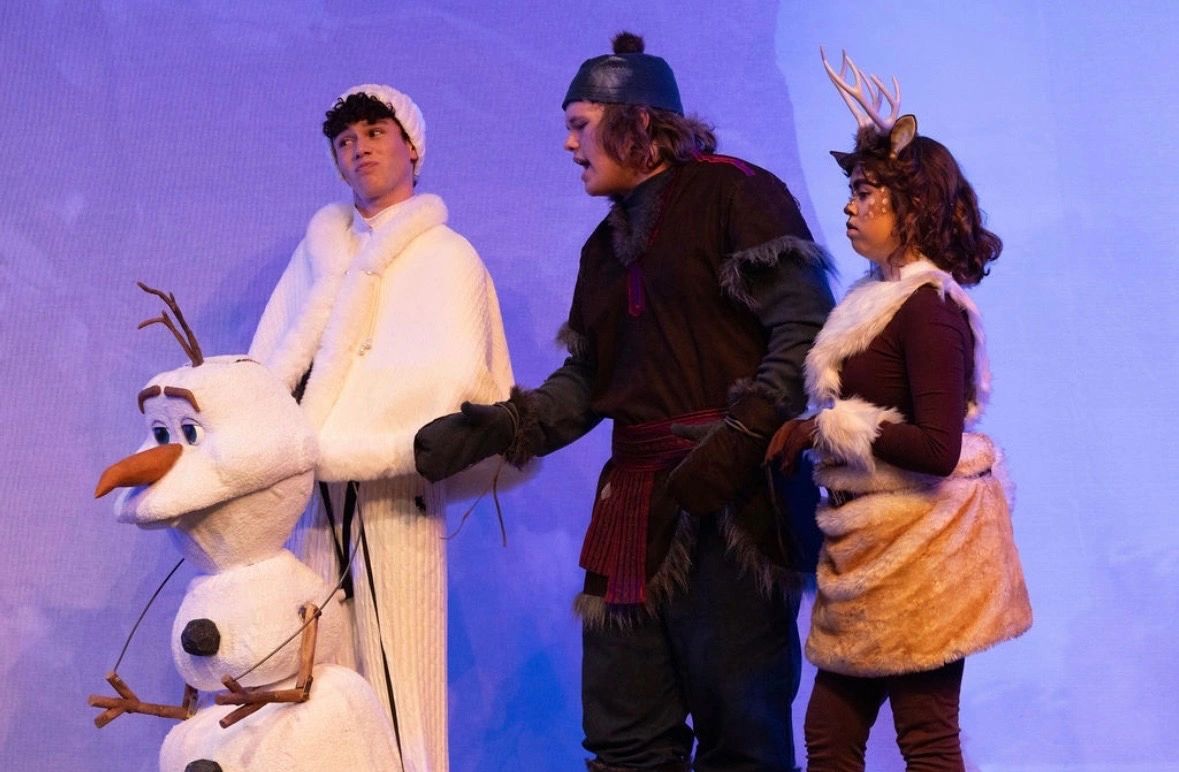 Three actors in winter-themed costumes on stage.