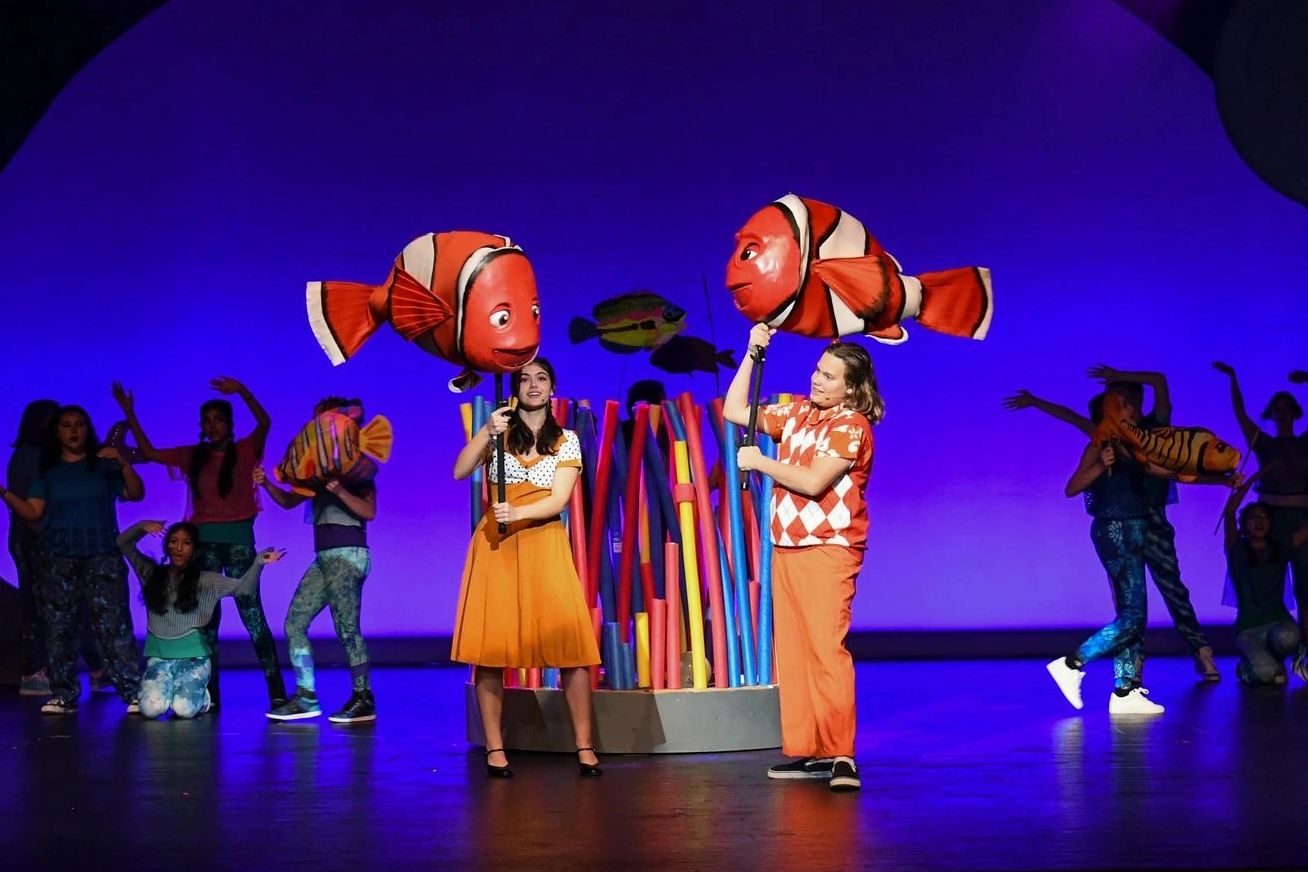 Two performers hold clownfish puppets during a colorful stage play.