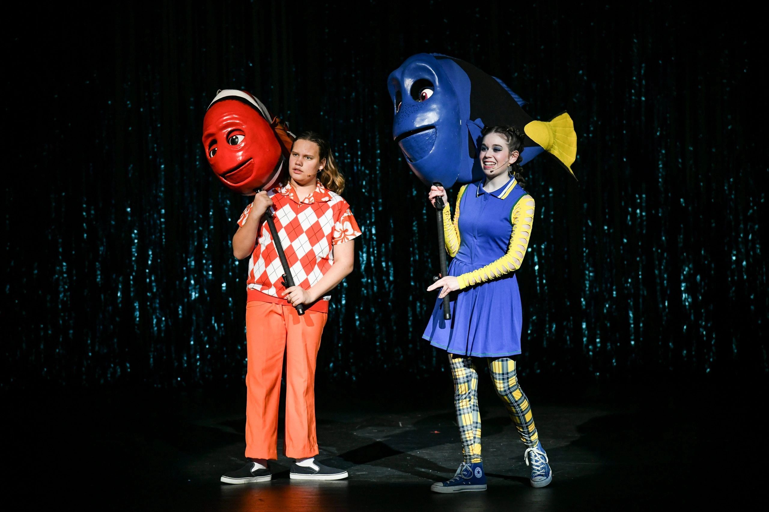 Two performers with large fish head props on stage.