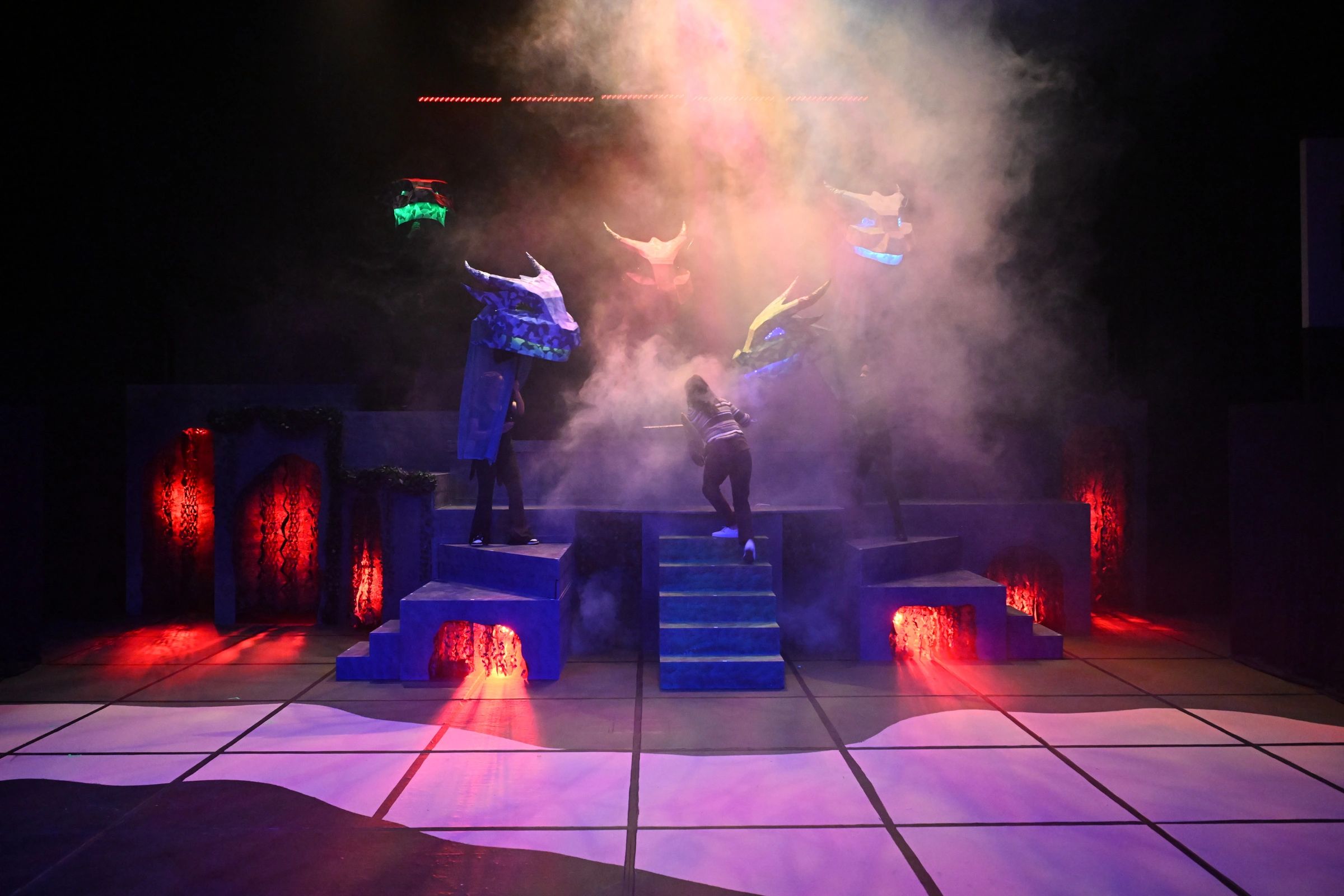 Theatrical dragon heads with colorful lighting and fog effects on stage.