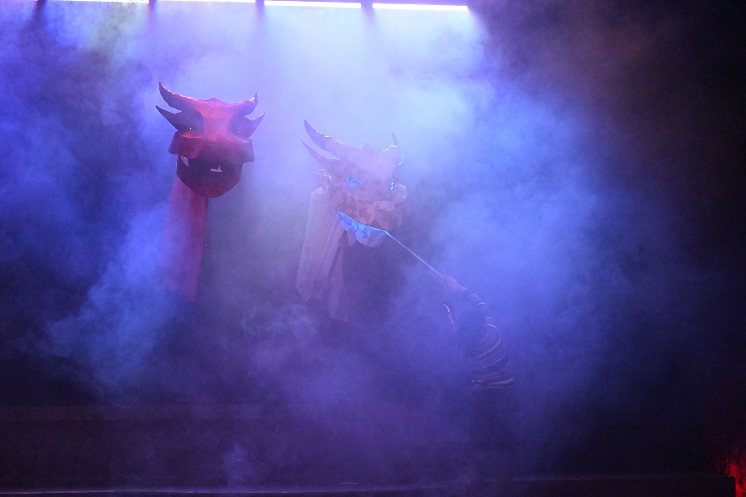 Two large dragon puppets on a smoky stage with a person manipulating one.