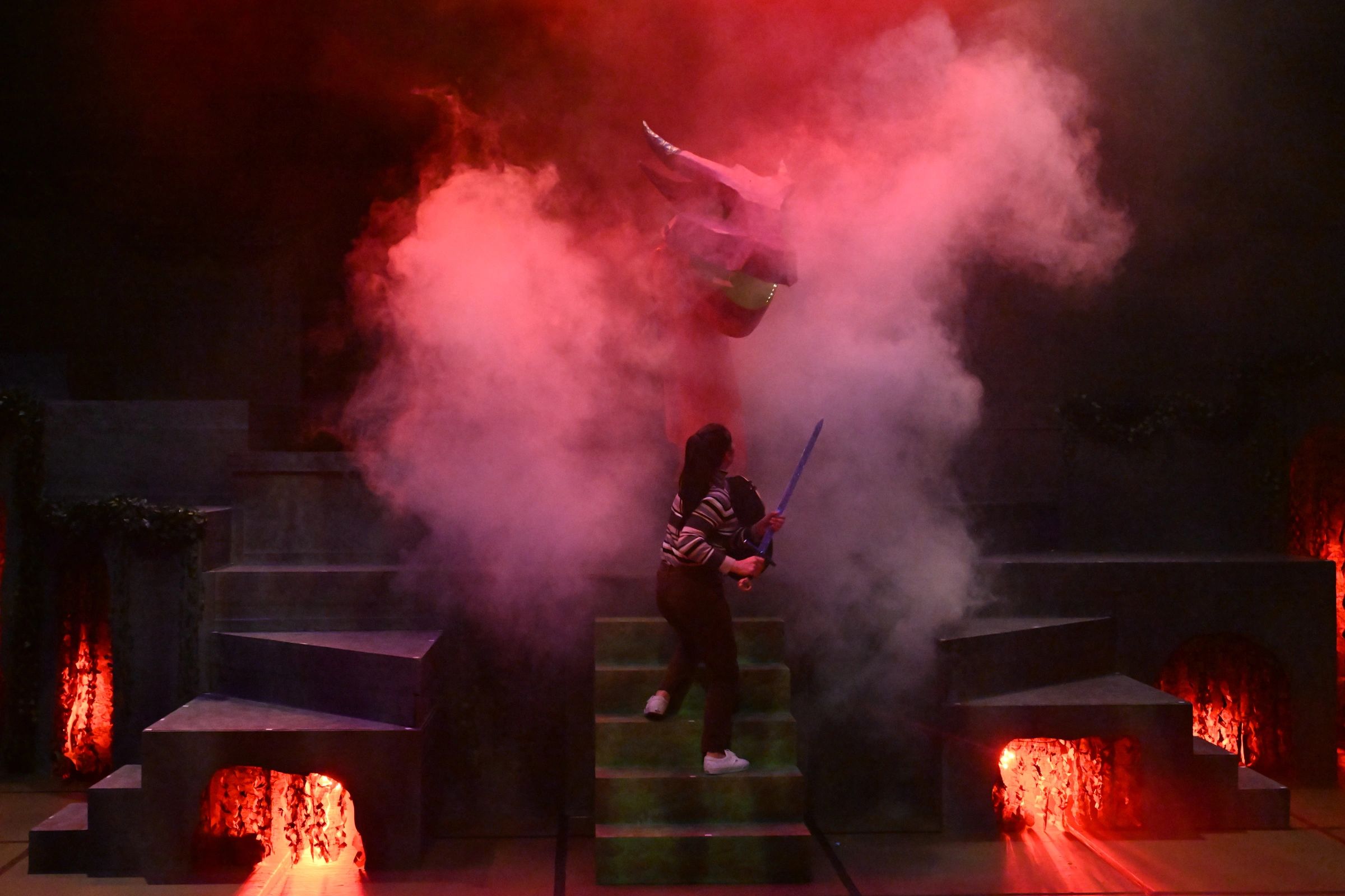 A person faces a smoky red-lit dragon figure with a sword.
