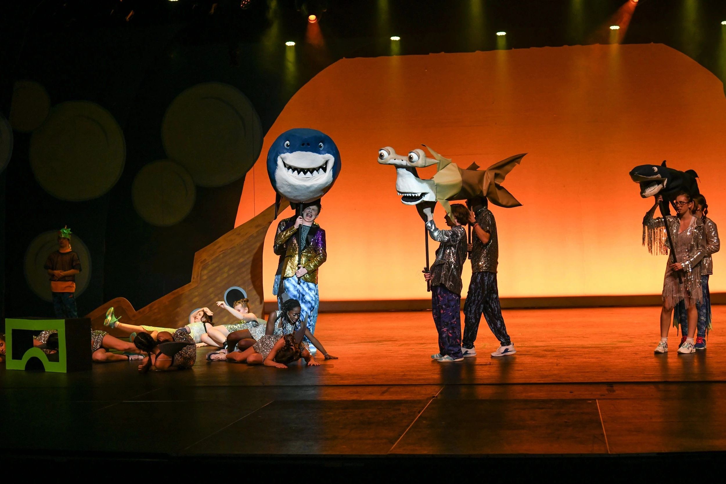 Children performing with shark puppets on stage.