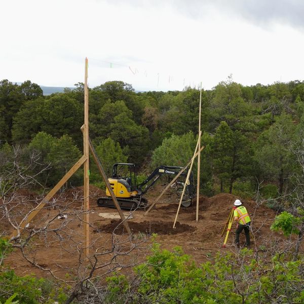 Construction worker surveying a forested excavation site with machinery.