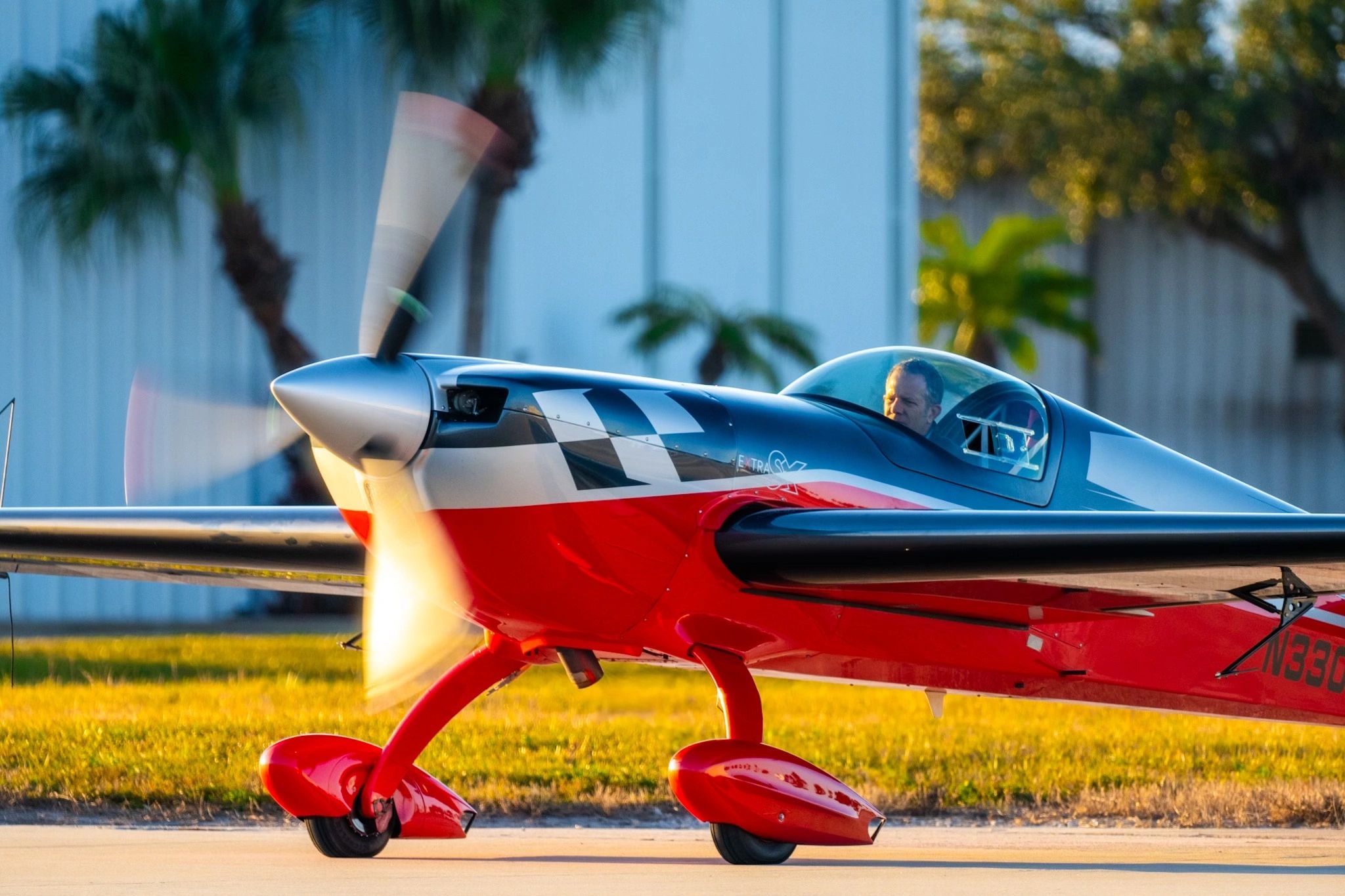 A red and black propeller airplane on the runway with a pilot inside.