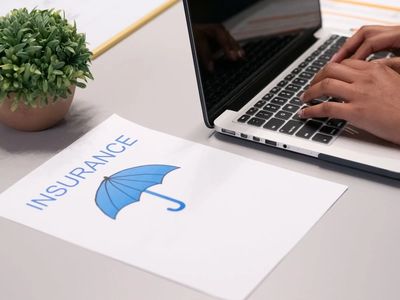 Insurance concept with umbrella on notepad, a plant and laptop.