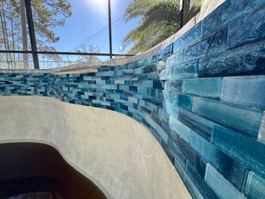 Curved wall with blue-tiled mosaic under natural light and palm trees.