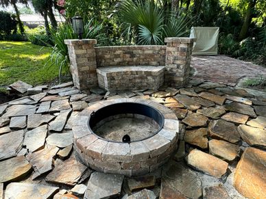 Stone fire pit with curved bench in a lush garden setting.