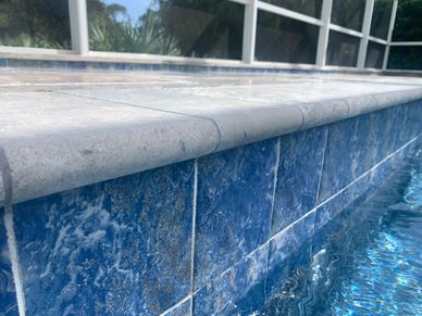 Close-up of a tiled pool edge with water reflecting on blue tiles.