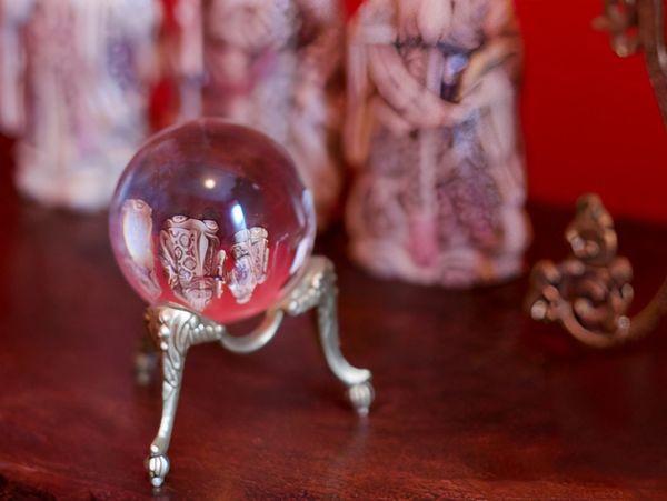 A clear crystal ball resting on a decorative antique gold stand on a wooden surface.