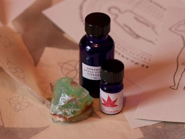 Small dark bottles of essential oil and a clear crystal resting on a wooden surface.