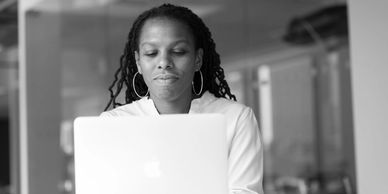 a woman in a white top working on a laptop 