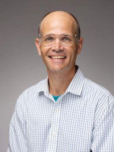 Smiling man wearing glasses and a checkered shirt.