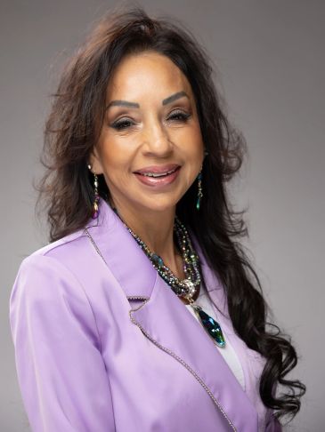 Woman smiling in a lavender blazer with jewelry.