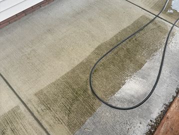 Concrete surface being cleaned with a pressure washer, showing a clear clean line.