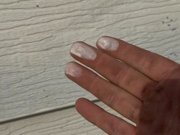 Fingers with white paint spots against a textured wall.