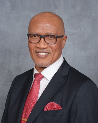 Professional man in suit, red tie, and glasses smiling in front of a gray background.