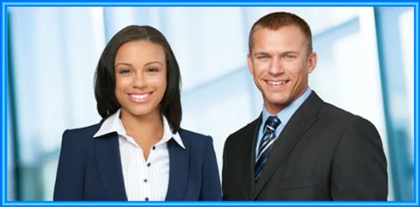 Two professionals smiling, dressed in business attire against a blurred office background.