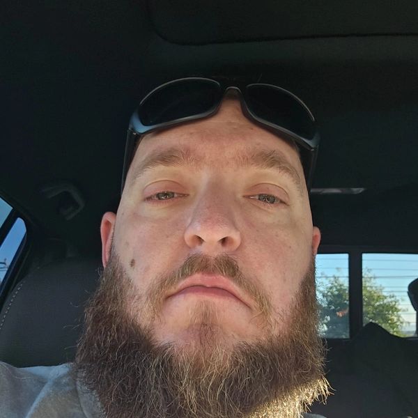 Man with a full beard and sunglasses on his head inside a vehicle.