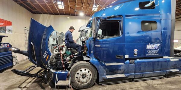 Mechanic performing maintenance work on truck in open engine hood