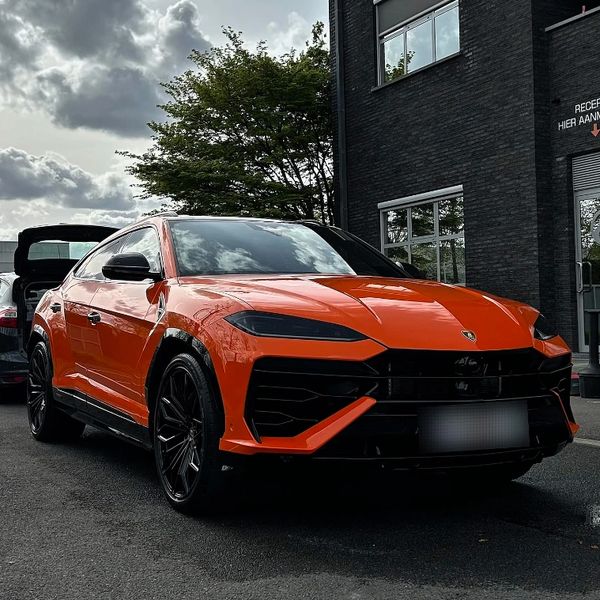 Orange Lamborghini Urus parked on a street near a building.