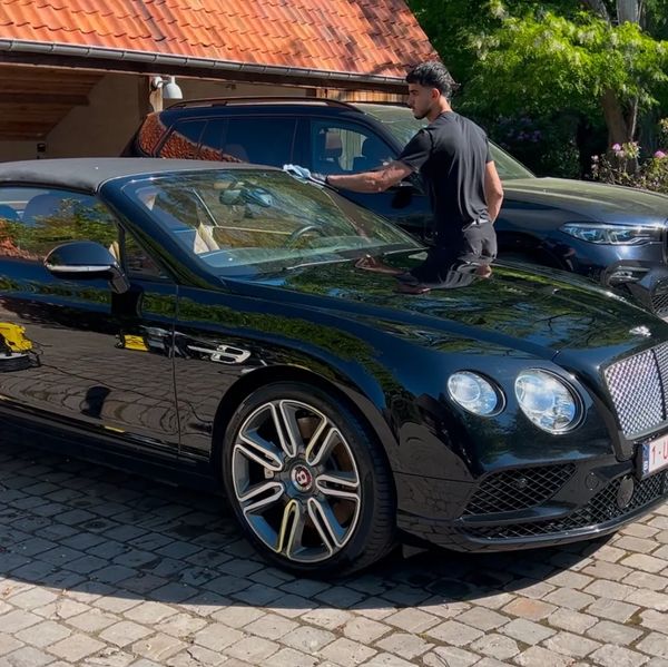 Man polishing a sleek black Bentley convertible in sunlight.