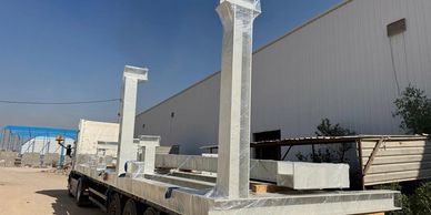 Metal framework structure loaded on a trailer against a warehouse background.
