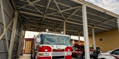 Fire trucks parked under a large metal canopy at a fire station.