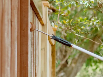 Painting a wooden fence with a roller brush in a garden.