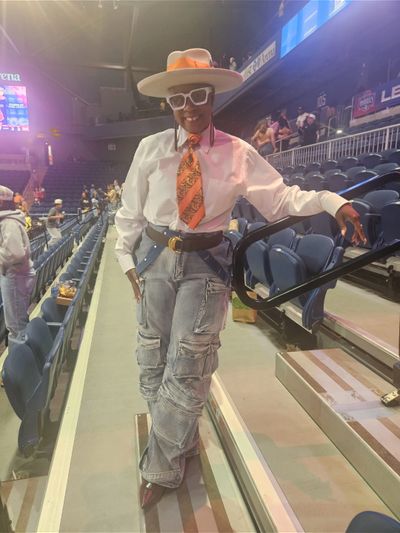 Person in stylish hat, white shirt, orange tie, and cargo jeans at an event.