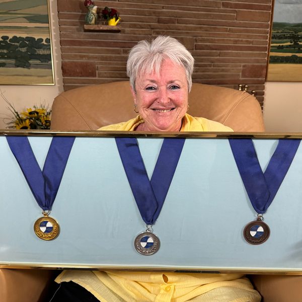 Smiling woman proudly displays three medals in a framed case.