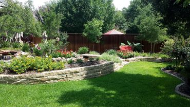 A lush garden with stone retaining walls and vibrant flowers under bright sunlight.