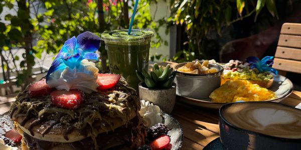 A delicious brunch setup with pancakes, eggs, avocado toast, and drinks on a sunny table.