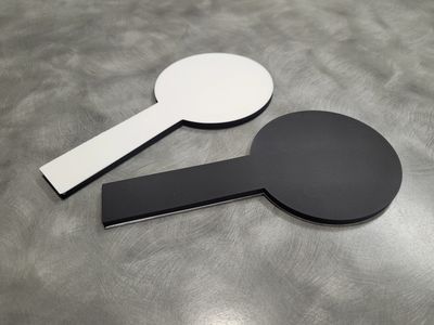 Premium EziFind Coasters, one with white side up, the other with black side up on a grey benchtop.