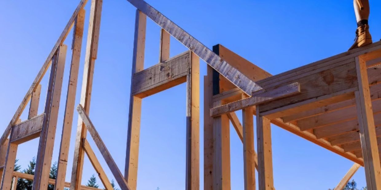 Wooden frame structure of a house under construction against a clear blue sky.