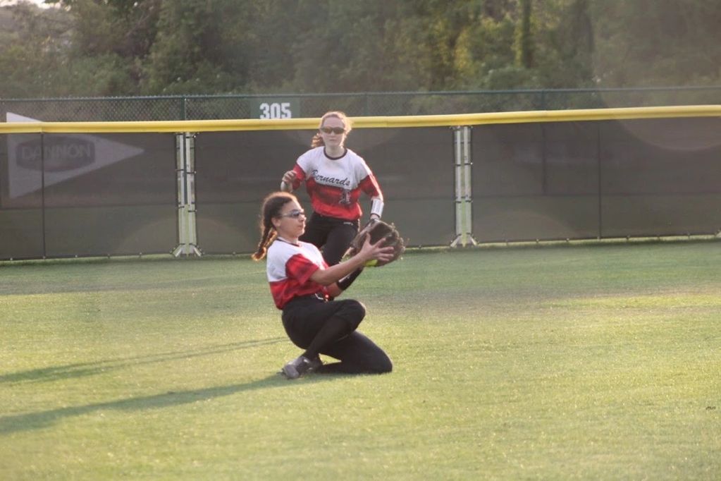 Girl softball player catches ball on one knee during a game.