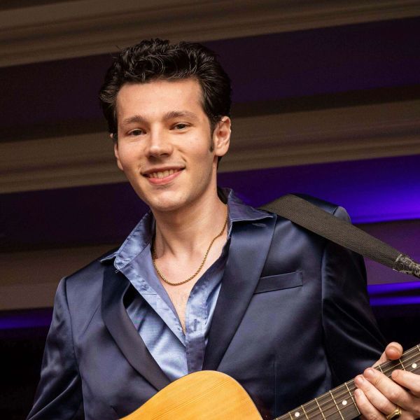 Young man smiling with guitar in a satin suit.