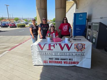 Four women stand behind a VFW veterans welcome table outdoors.