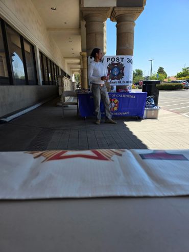 Person standing near a table with a Veterans of Foreign Wars banner outside a building.