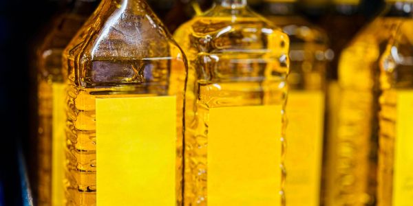 Rows of clear plastic bottles filled with golden cooking oil with blank yellow labels.