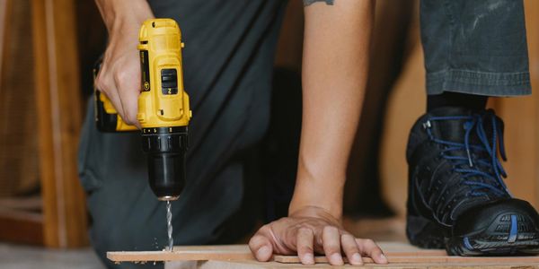 Person using a yellow power drill on wood while kneeling.